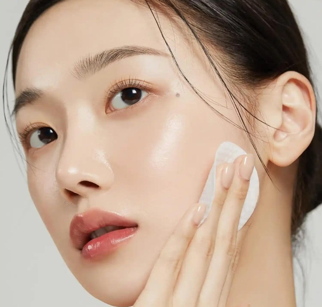 Woman applying cream to her face with a neutral background