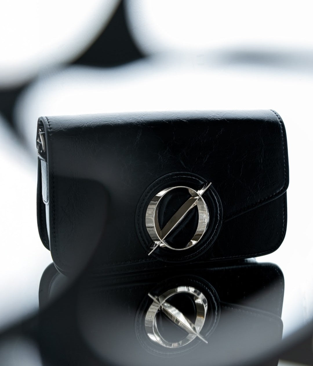 Black clutch bag with a logo on a reflective surface
