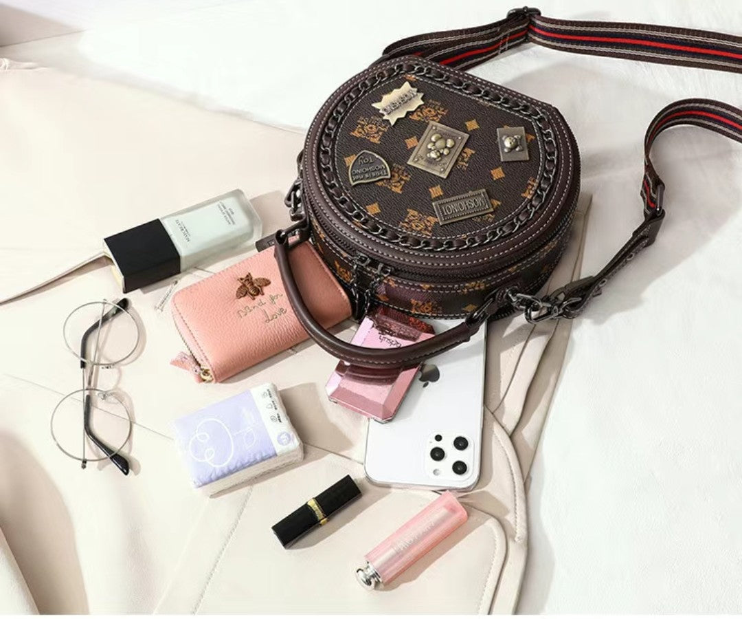 Round brown handbag with decorative patterns on a white surface with accessories around it.