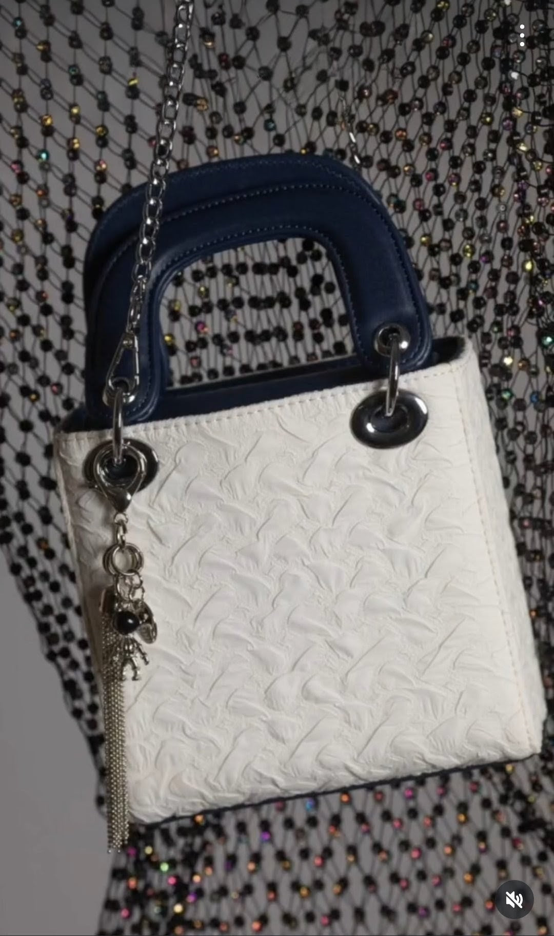 White textured handbag with blue handle and chain detail on a patterned background