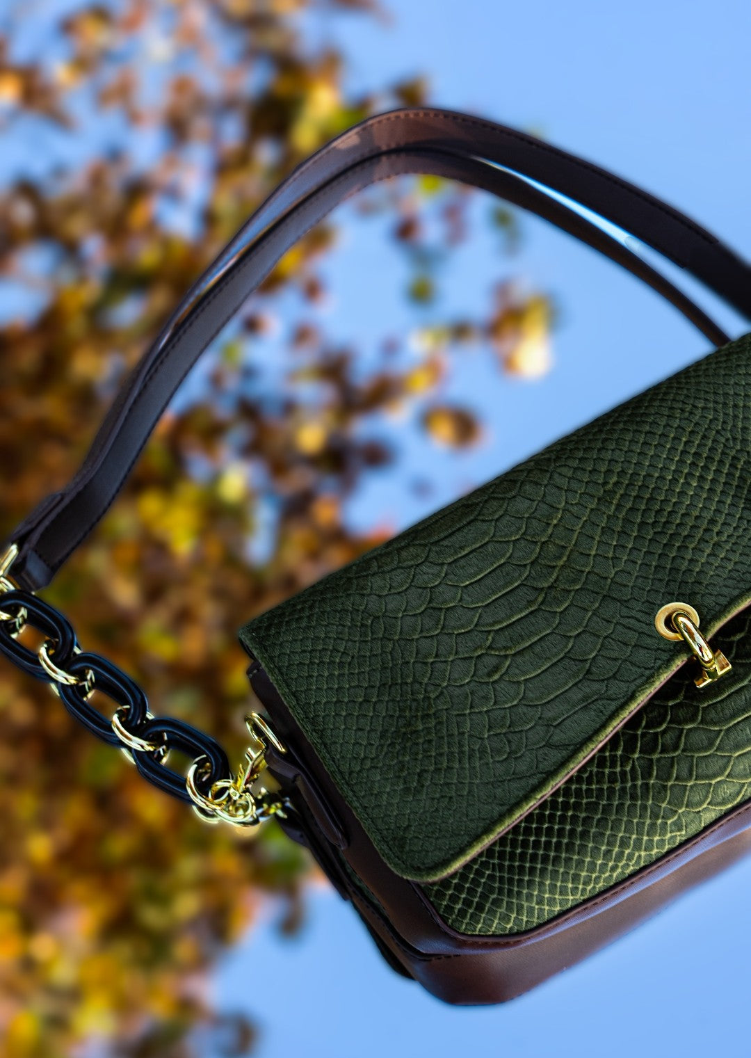 Green handbag with gold accents against a blurred natural background