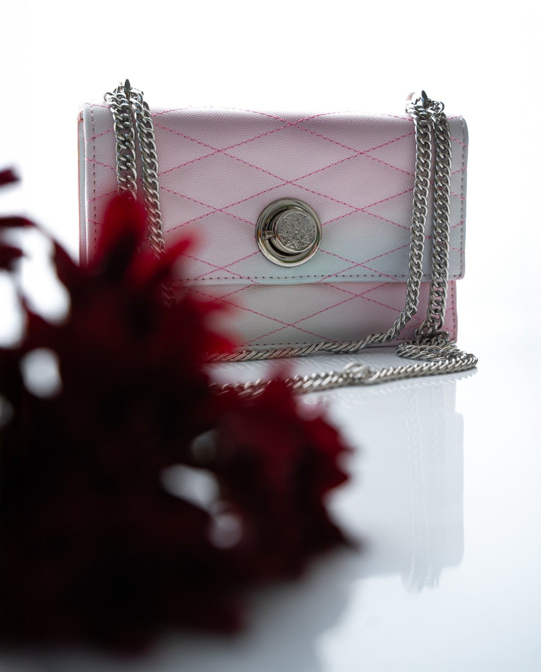 Pink quilted handbag with a chain strap on a white background