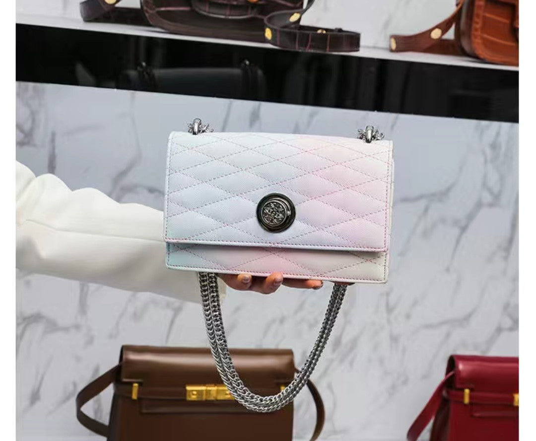Iridescent handbag with chain strap held by a hand against a marble background