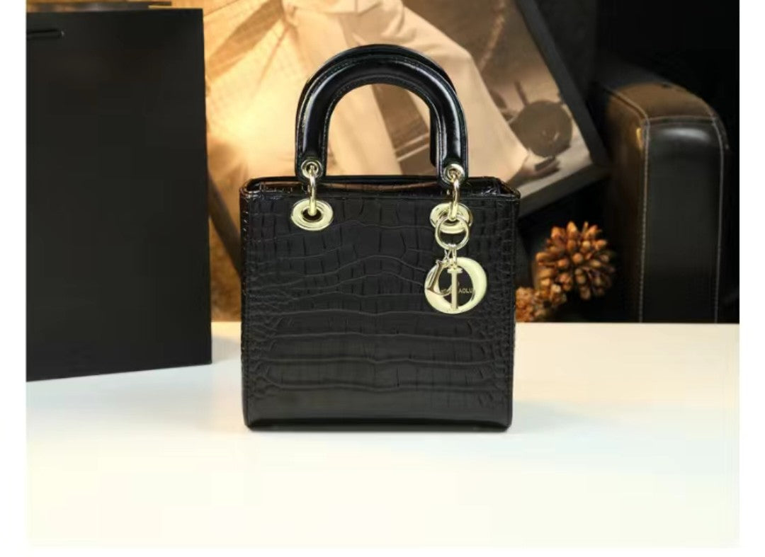 Black crocodile-patterned handbag with gold hardware on a white surface.