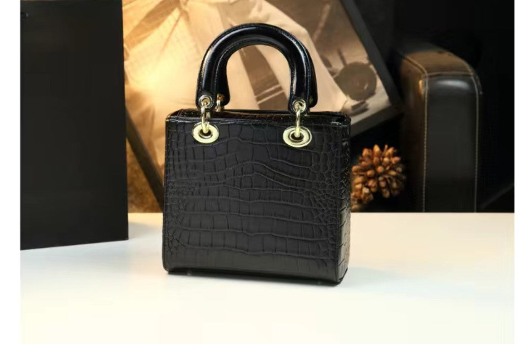 Black crocodile-patterned handbag with gold accents on a reflective surface