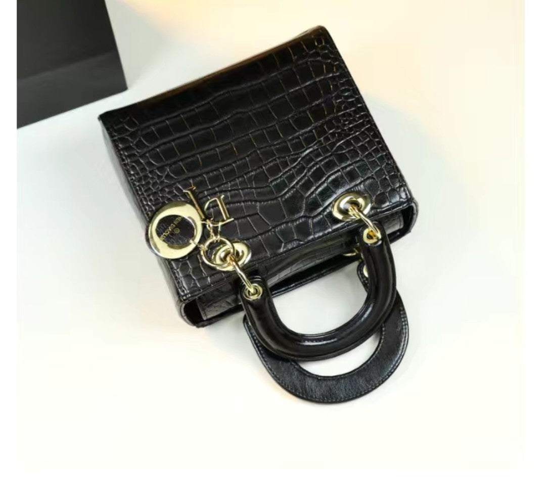 Black crocodile-patterned handbag with gold hardware on a white background
