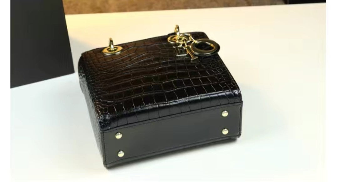 Black crocodile-patterned handbag with gold accents on a white surface