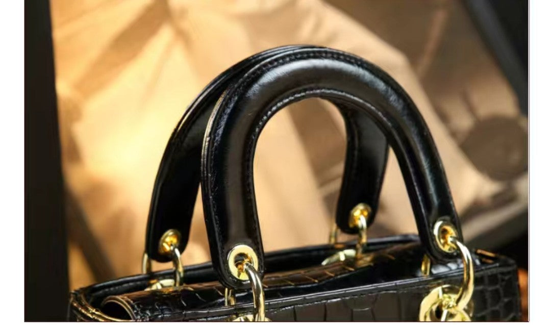 Close-up of a black handbag handle with gold hardware on a beige background