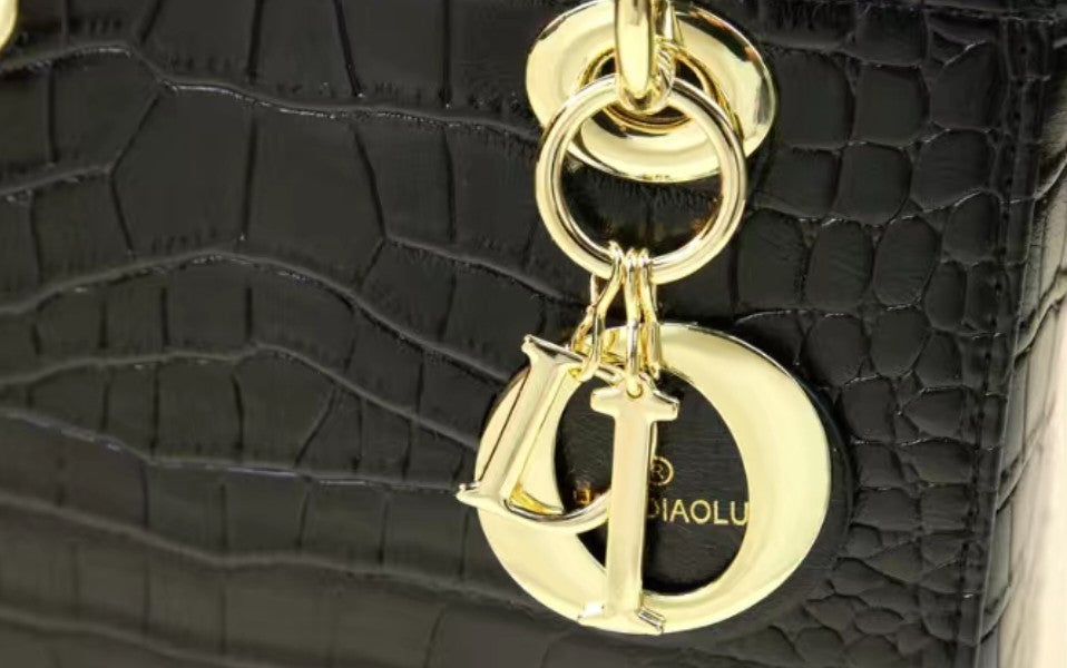 Black textured handbag with a gold keychain featuring a logo.