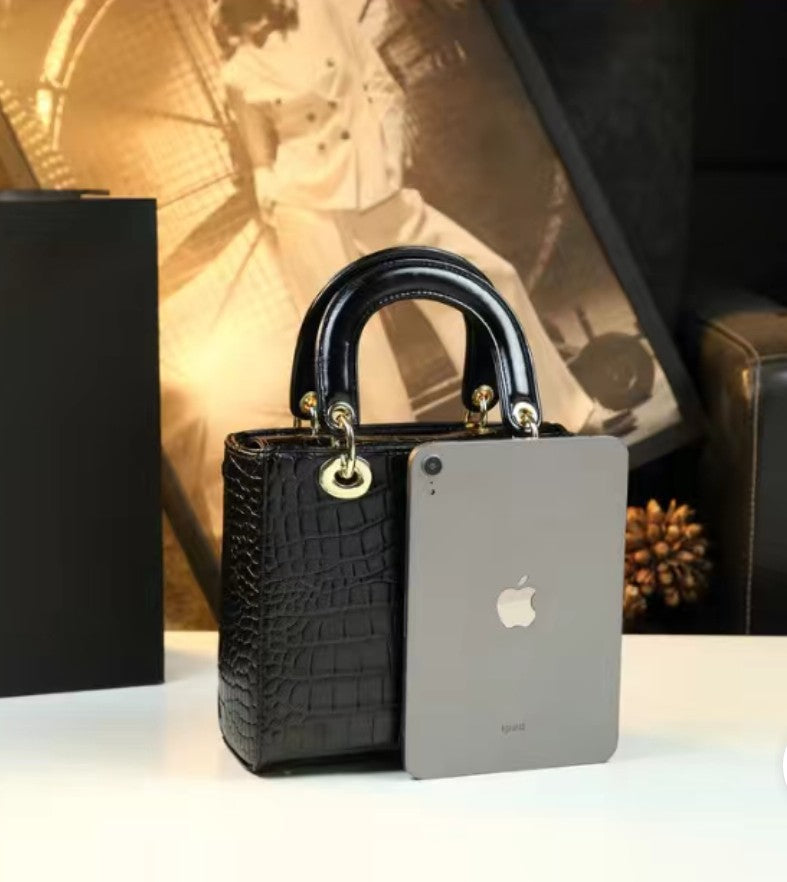 Black handbag with gold accents next to a silver phone on a white surface.