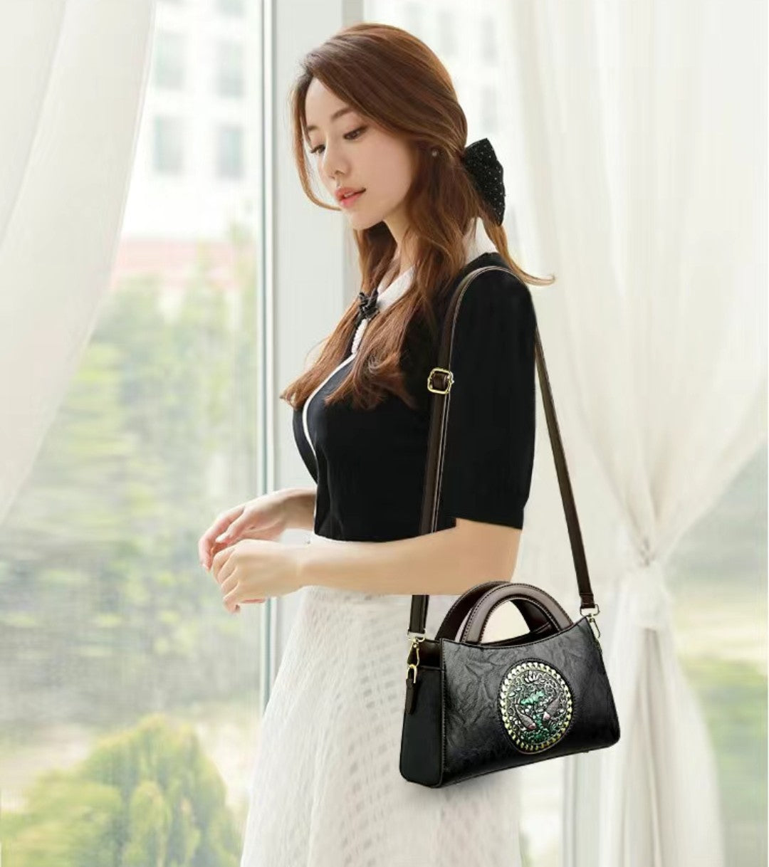 Woman holding a black handbag with decorative elements in a bright room.