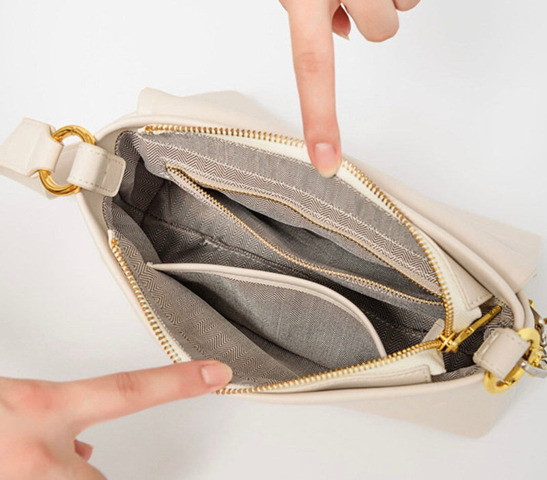 Close-up of a beige handbag with gold zipper and interior lining, showing a finger pointing inside.