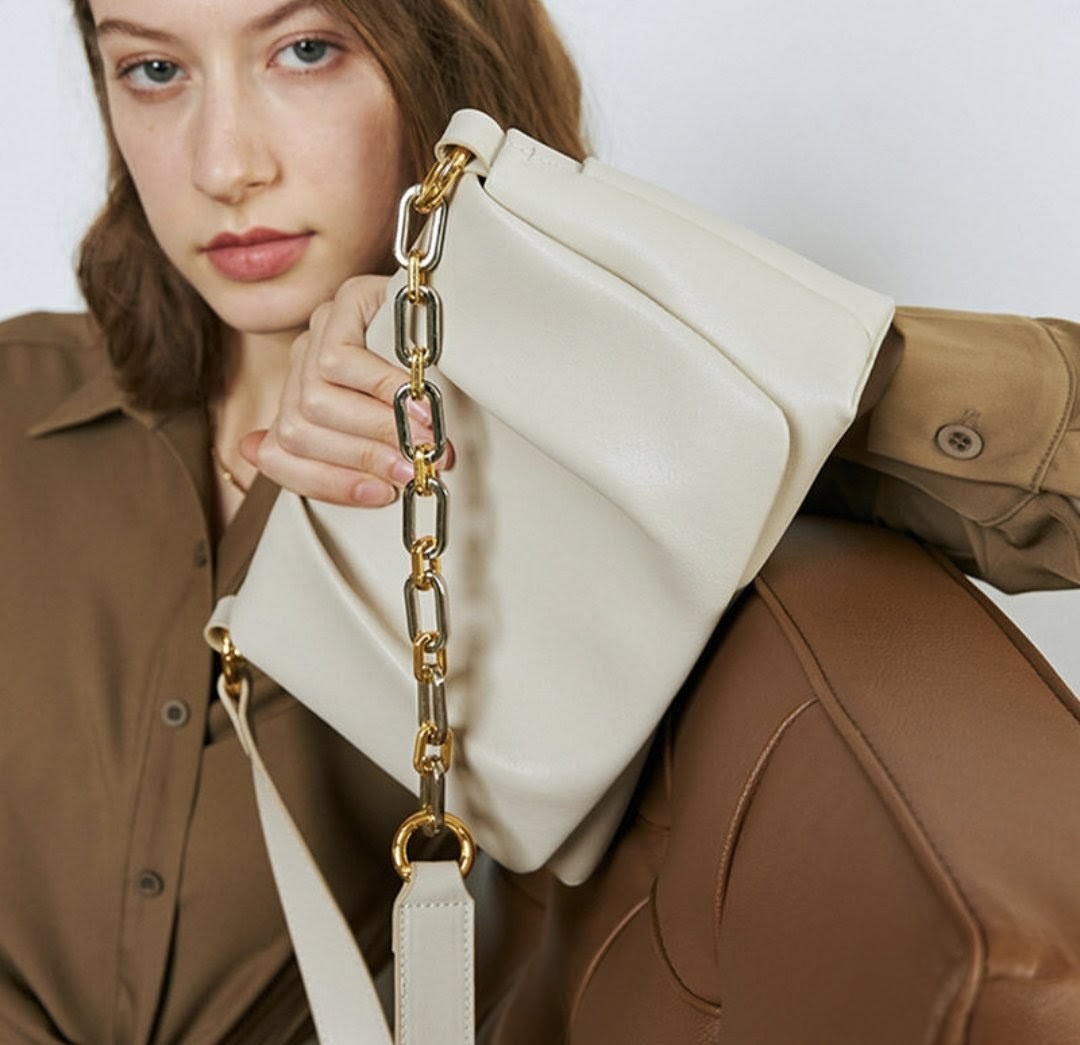 Person holding a beige handbag with gold chain strap against a neutral background