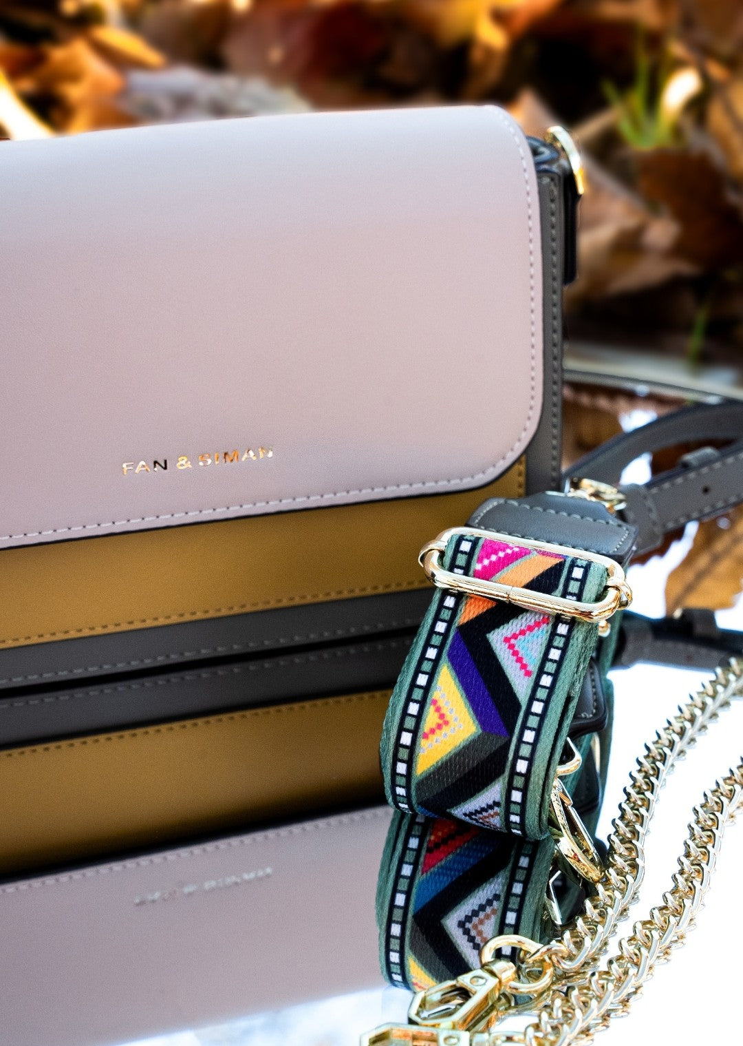 Handbag with a colorful strap on a blurred natural background