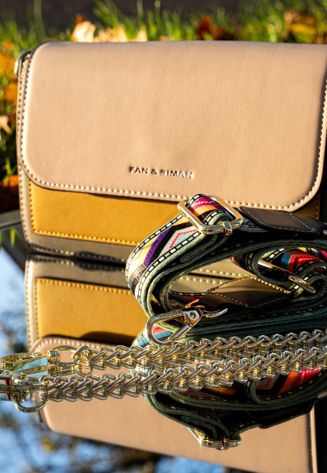 Beige handbag with a colorful strap on a reflective surface
