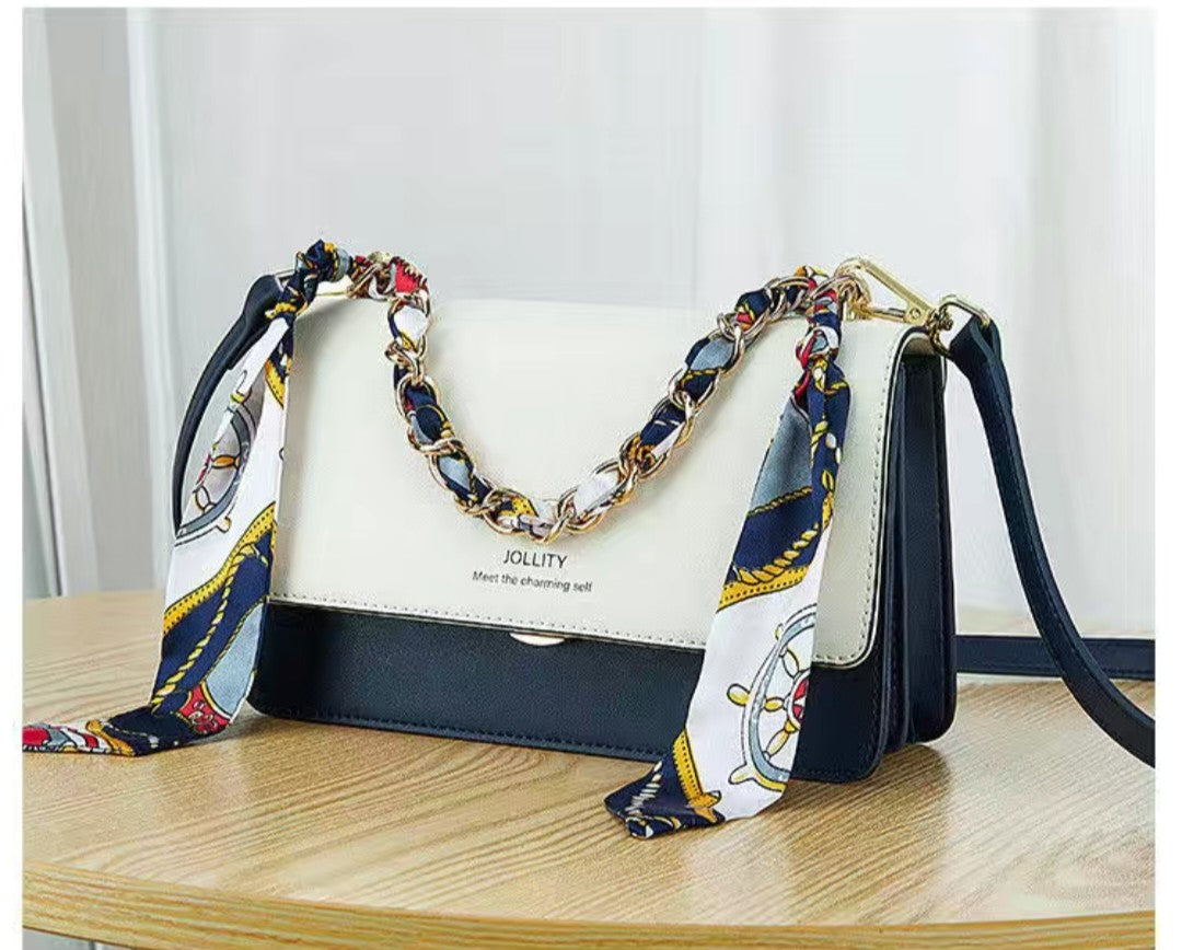 White handbag with a decorative chain and scarf on a wooden surface