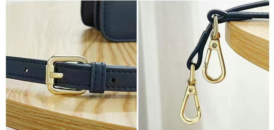 Close-up of a navy leather strap with gold buckle and matching carabiner on a wooden surface.