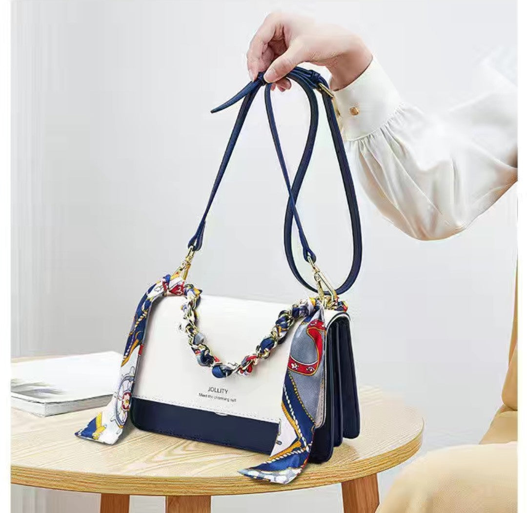 White handbag with blue accents and a decorative strap held by a person.