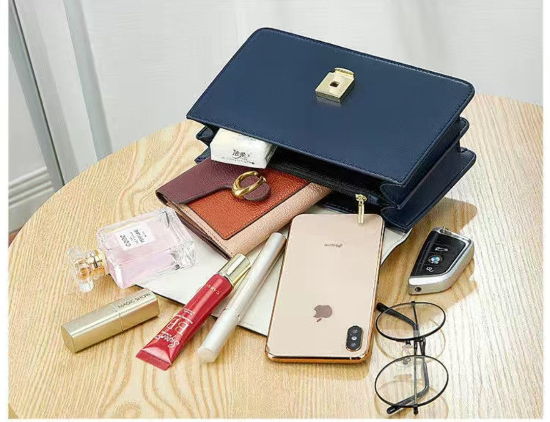 Open navy blue handbag with various items including a phone, glasses, and cosmetics on a wooden surface.