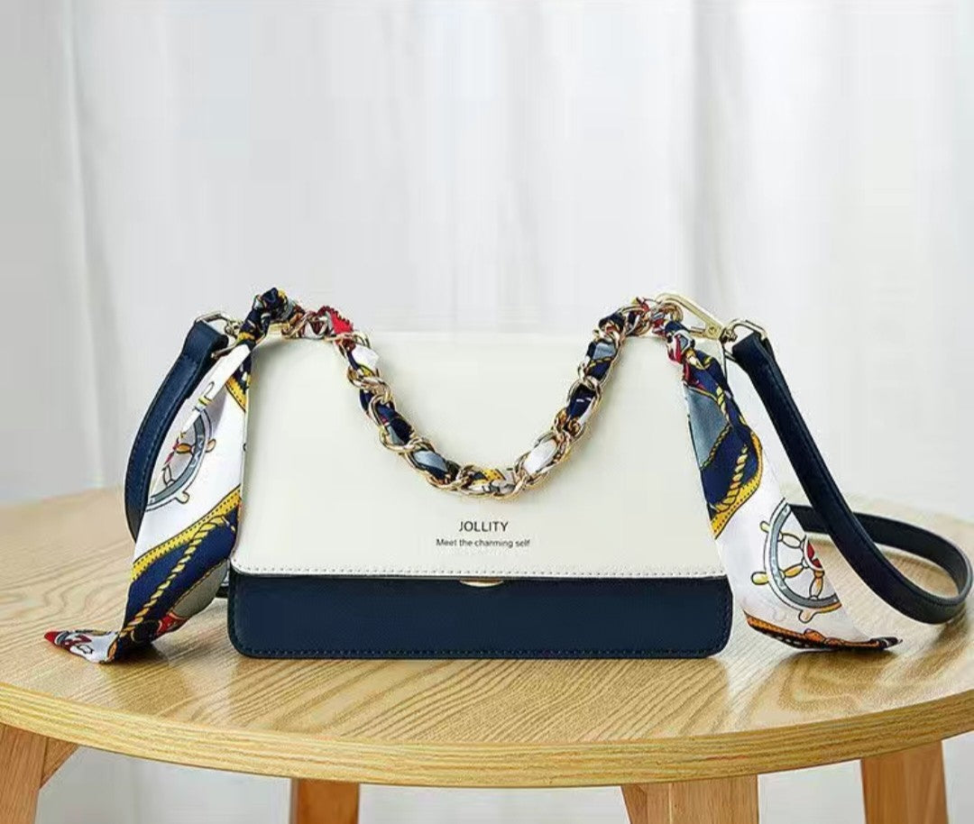 White and navy handbag with colorful chain handle on a wooden table