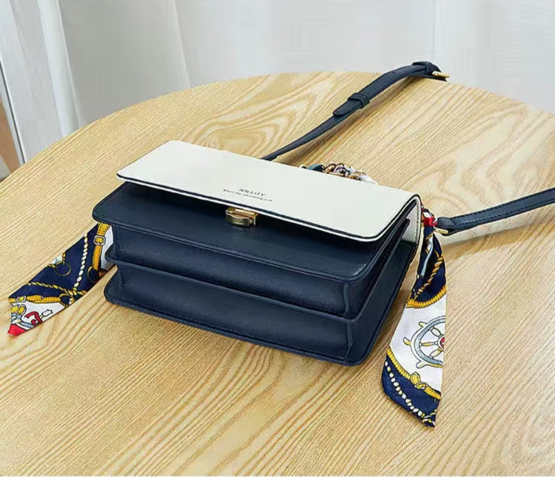 Navy blue handbag with a white flap and decorative strap on a wooden surface