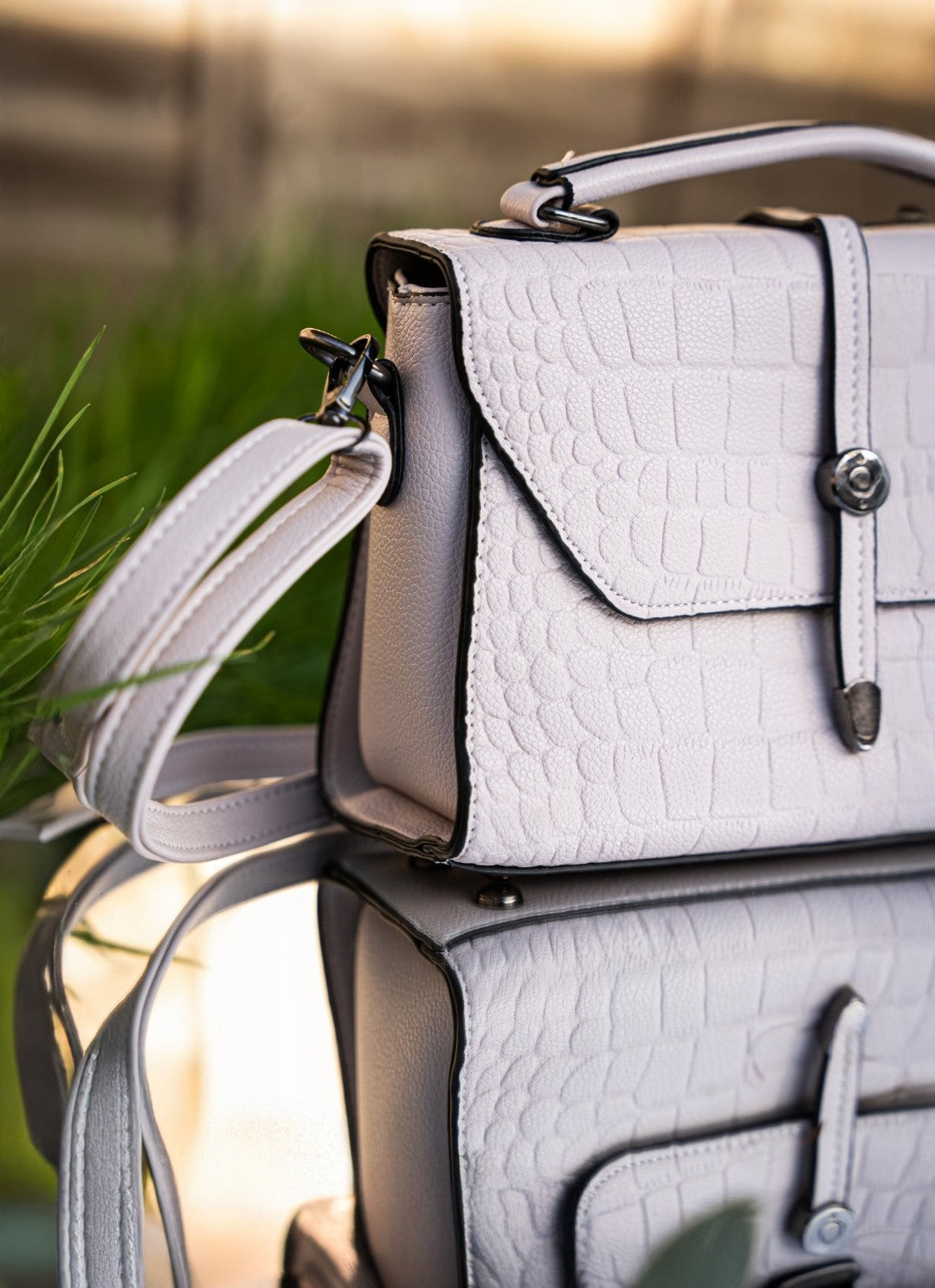 White textured handbag with a strap against a blurred natural background
