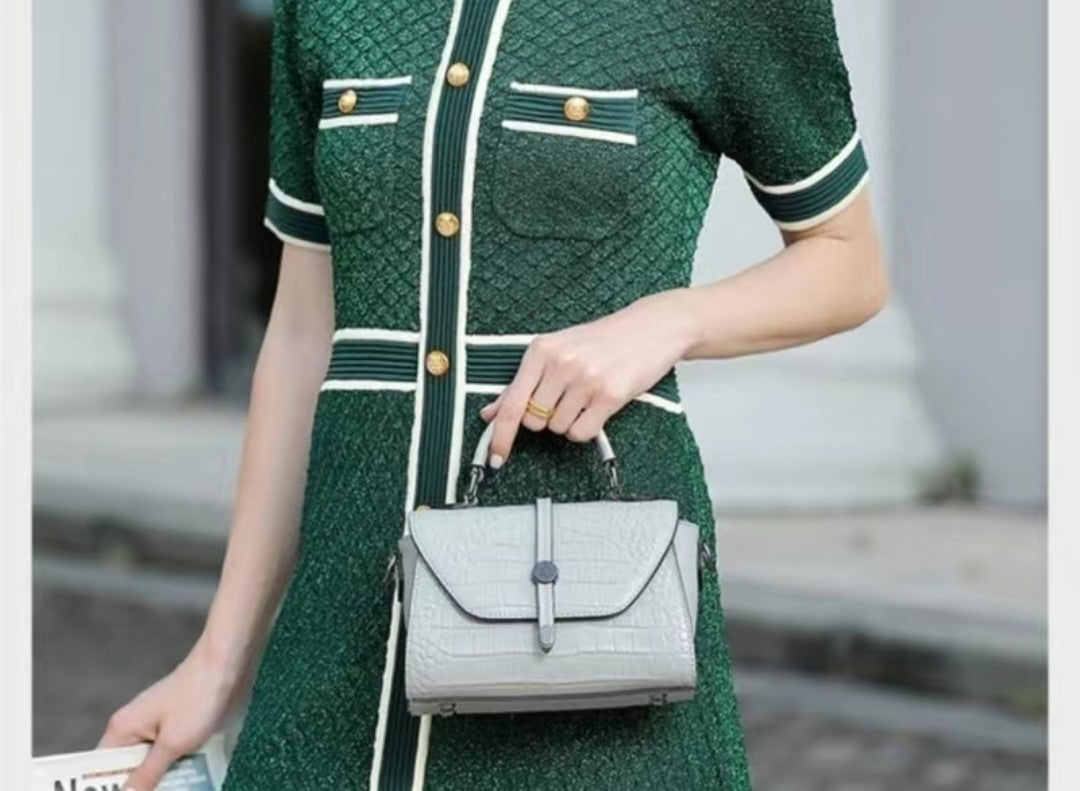 Person wearing a green dress with white accents, holding a gray handbag.