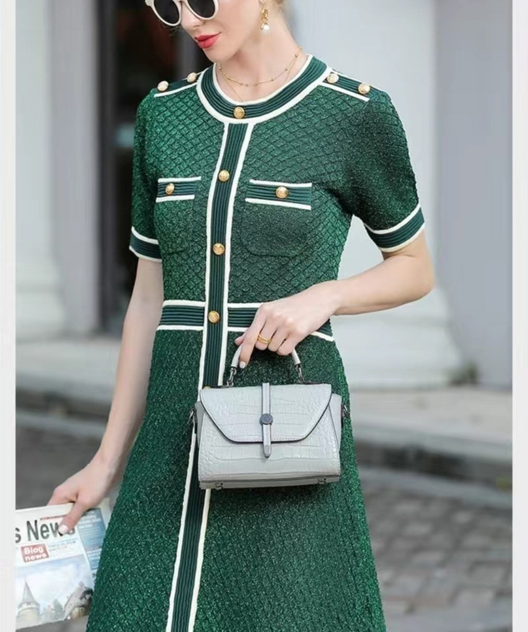 Woman in a green dress with white accents holding a gray handbag.