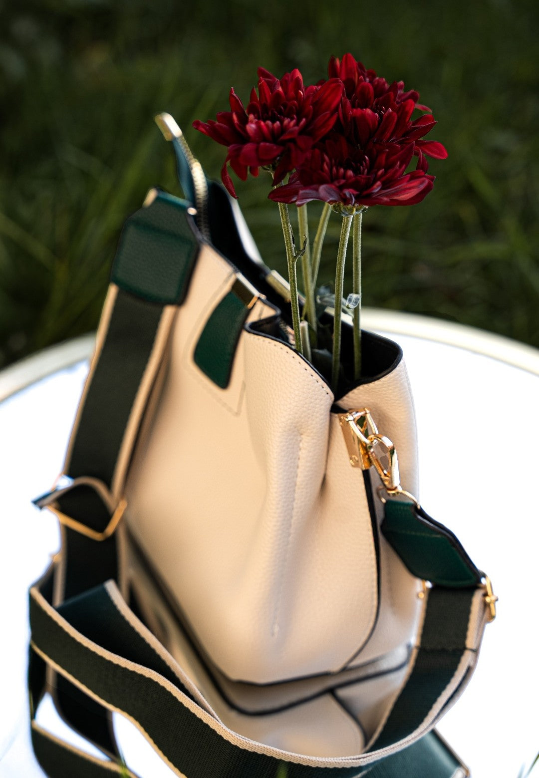 Beige handbag with green accents holding red flowers on a reflective surface.