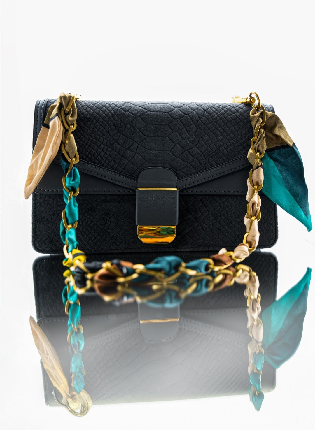 Black handbag with gold chain strap on a reflective surface