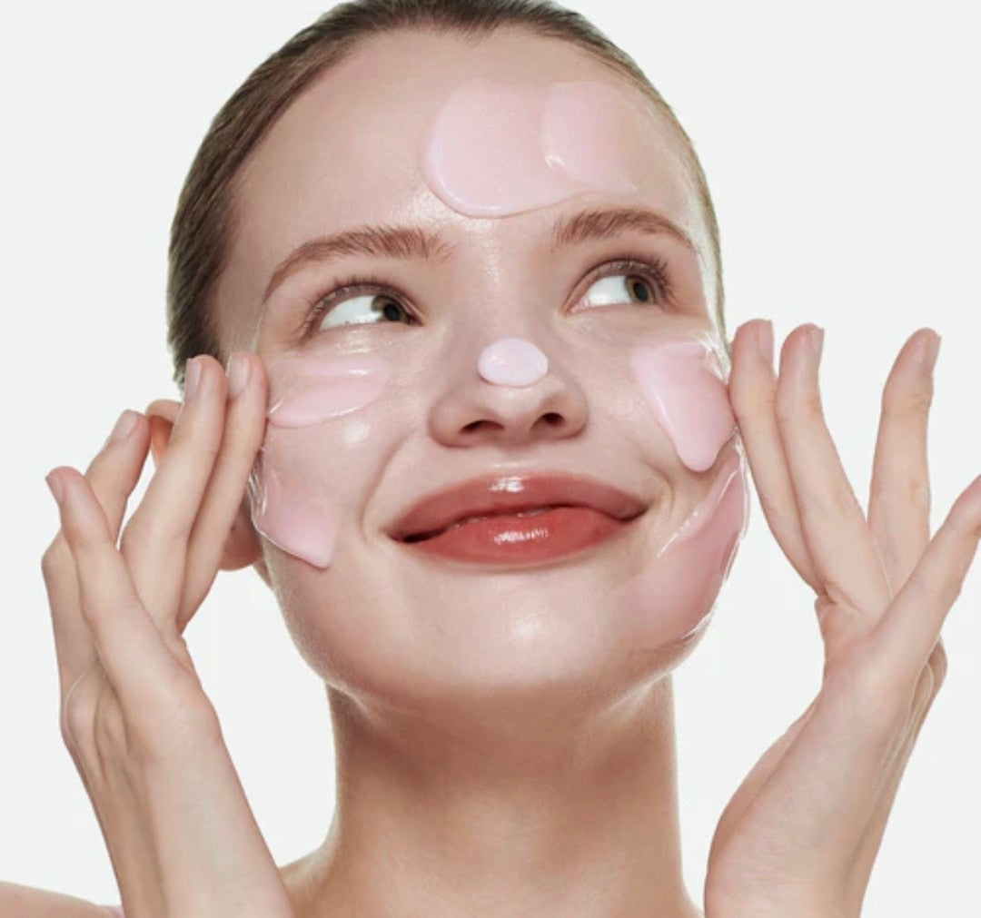Woman applying pink face masks to her face against a light background
