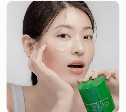 Woman applying cream to her face with a green skincare product in the foreground