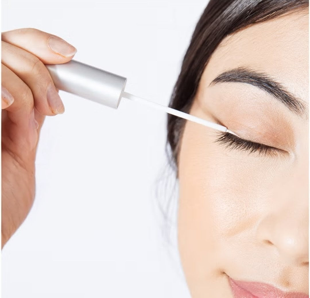 Person applying eyelash serum with a small applicator on a white background
