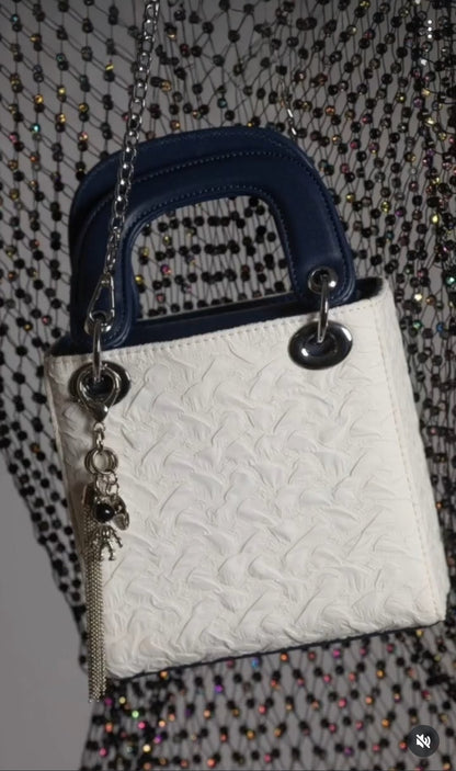 White textured handbag with blue handle and chain detail on a patterned background