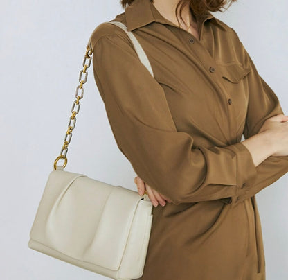 Person wearing a brown coat holding a beige handbag with a gold chain strap on a light gray background