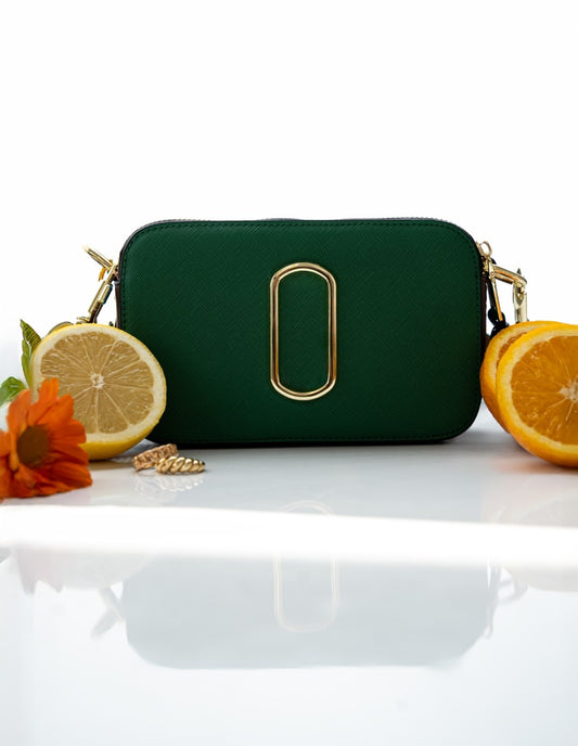 Green handbag with gold accents on a white surface with fruits and flowers.