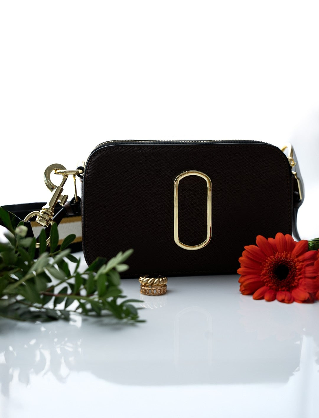Black handbag with gold accents on a white surface with flowers and greenery.