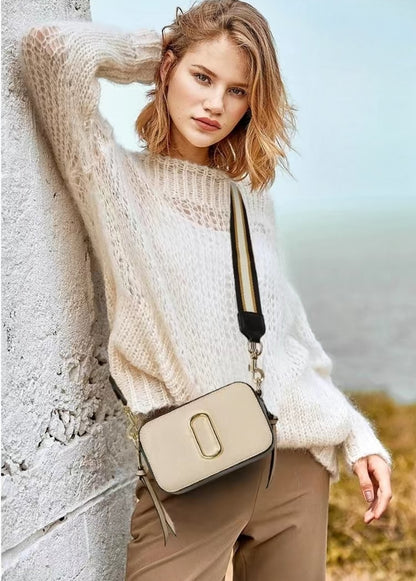 Woman wearing a beige sweater and carrying a matching handbag against a natural background