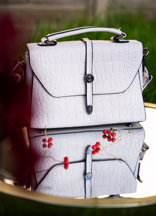White textured handbag with black accents on a reflective surface