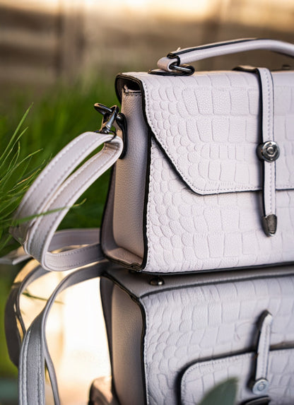 White textured handbag with a strap against a blurred natural background