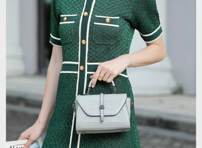 Person wearing a green dress with white accents, holding a gray handbag.