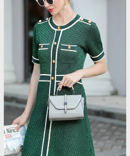 Woman in a green dress with white accents holding a gray handbag.