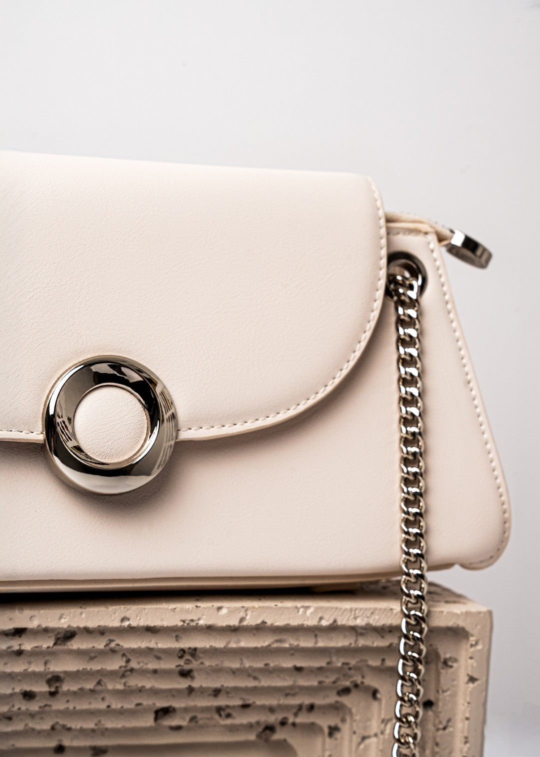 Beige handbag with a chain detail on a textured surface