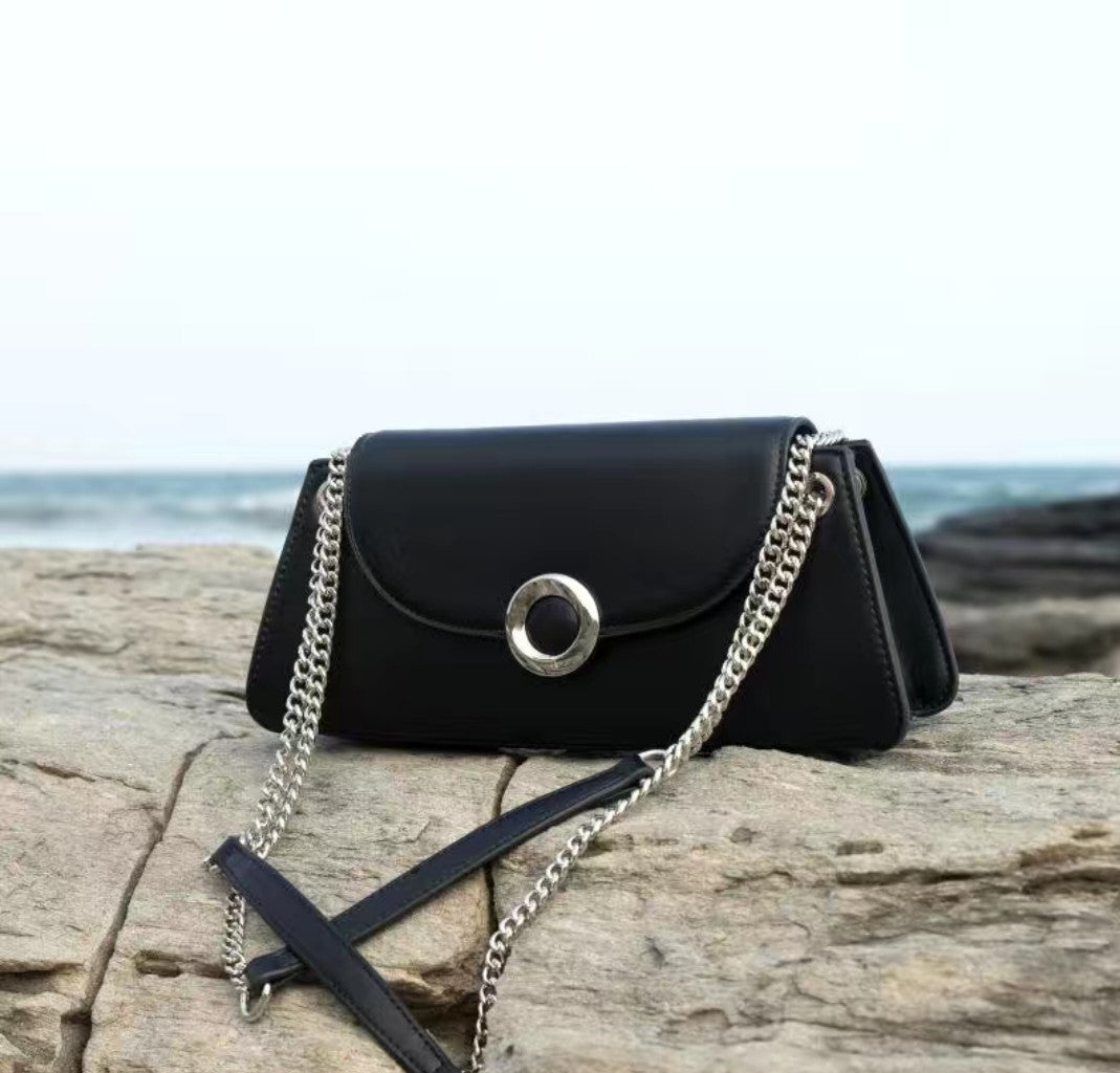 Black handbag with a chain strap on a wooden surface near the ocean.